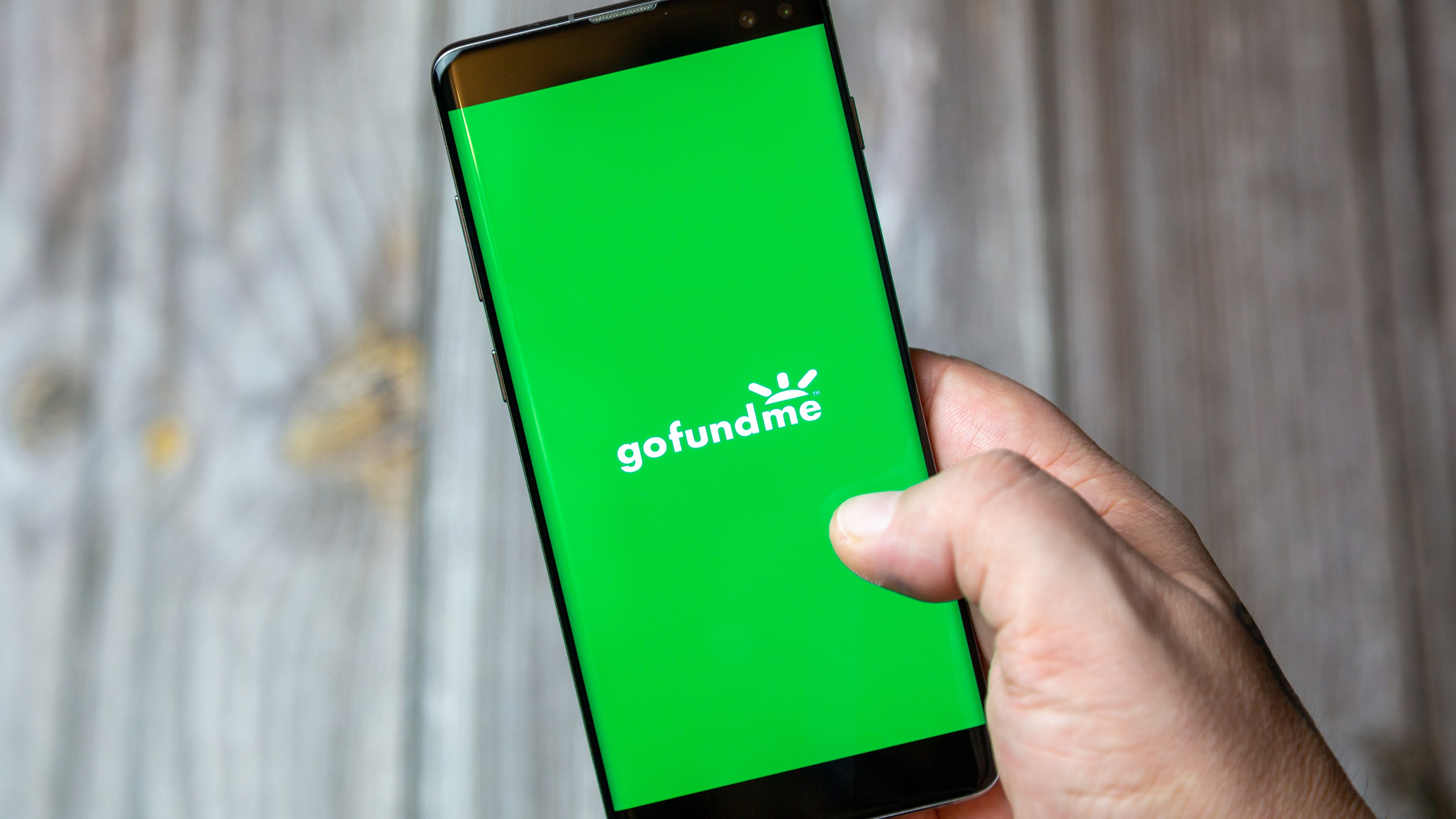 A mobile phone or cell phone being held by a hand with the Go Fund me app open on screen